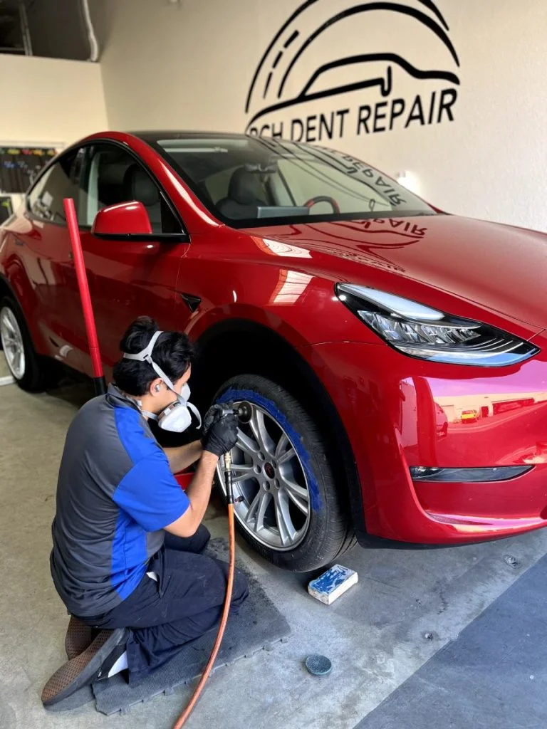 Technician refinishing the wheel of a red Tesla